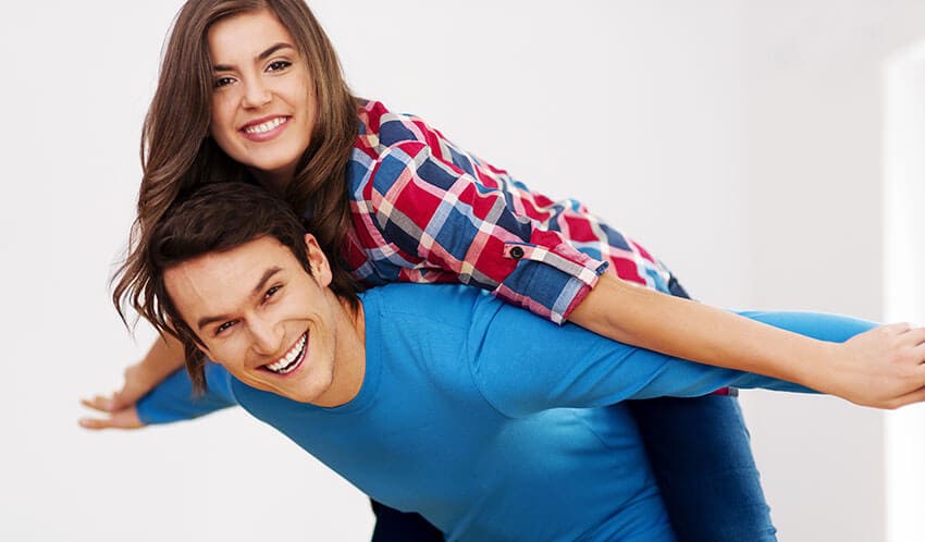 The image displays a scene in an outdoor driveway or yard, featuring a large, open-topped skip container constructed from metal, with a corrugated surface finish. The skip is predominantly grey, showing signs of use with some visible dirt and minor rust spots along the edges. It is positioned centrally in the foreground, with its longer side aligned parallel to the viewer. Behind the skip, a portion of a white commercial van with minimal branding is partially visible on the left side of the image, parked on a paved surface. In the background, a residential brick-built property with a tiled roof and white window frames can be seen, suggesting a suburban setting typical of Stoke on Trent or nearby areas. The environment appears to be a garage or garden area, with some scattered debris or waste materials adjacent to or partially inside the skip, indicating recent rubbish removal activity. The lighting is diffuse, consistent with an overcast sky, and the overall scene reflects a typical waste collection or clearance operation coordinated by Hire Man and Van as part of their removals service in the local area.